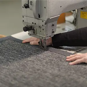 Foto eines Teppichs, der mit Nähmaschine eingefasst wird.