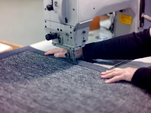Foto von der Seite von einem Teppich der gerade mit einer Bordüre vernäht wird.