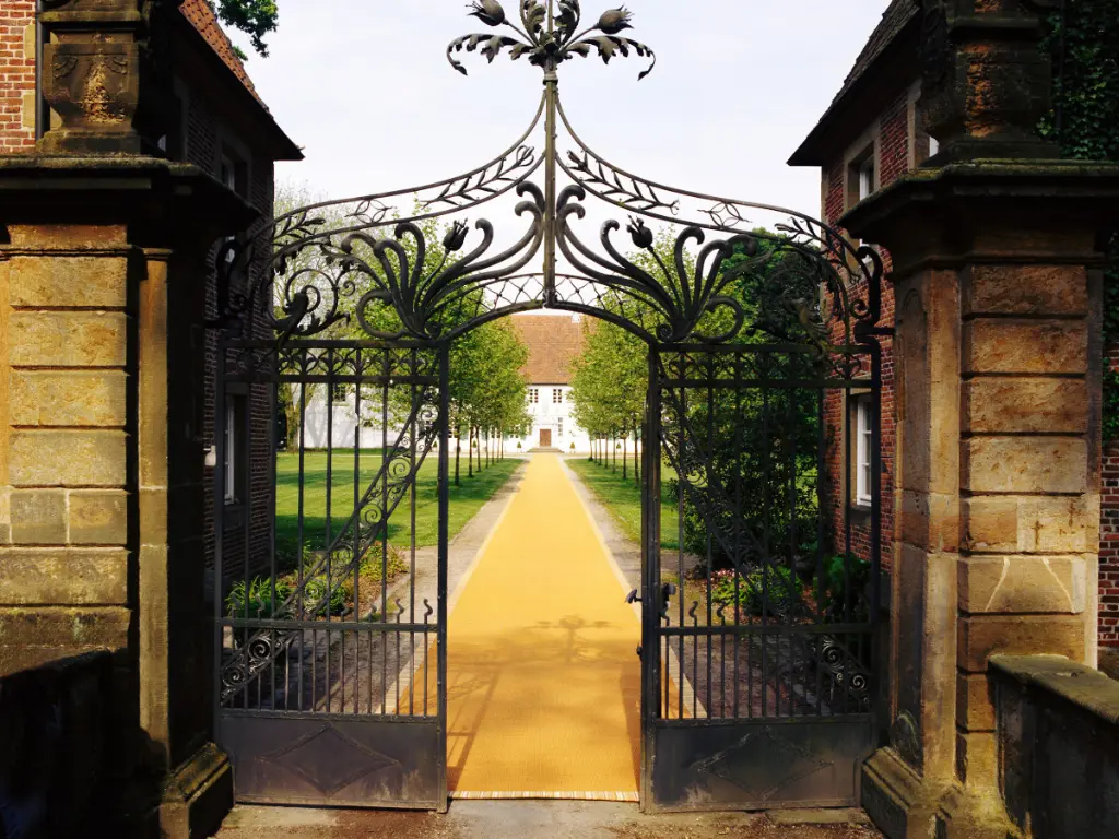 Foto eines Schlosses wo ein gelber Sisalteppich von DEKOWE vom Eisenthor bis zum Hauptgebäude hin führt.